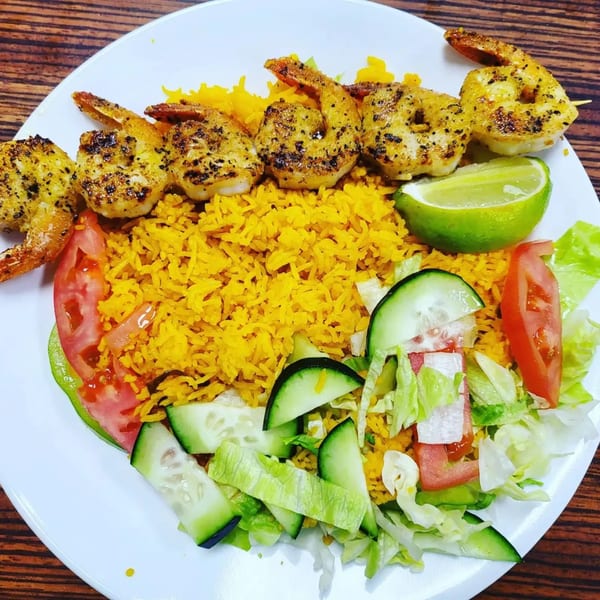 Grilled shrimp skewers with yellow rice, a side salad, and a lime wedge on a white plate.