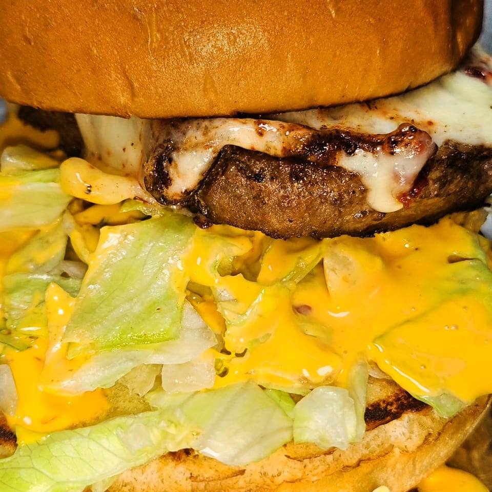 Close-up of a Big Apple's halal burger with melted cheese, lettuce, and sauce on a bun.