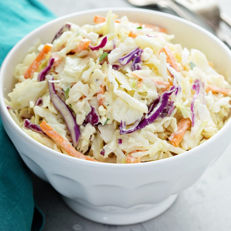 Close-up of a white bowl filled with creamy coleslaw, featuring shredded cabbage, carrots, and red cabbage.