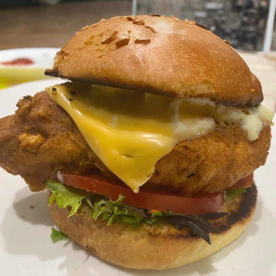 Halal fried chicken sandwich with melted cheese, lettuce, and tomato on a toasted bun.