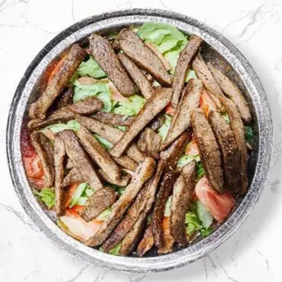 Halal gyro meat, lettuce, and tomatoes in a foil container on a white marble surface.