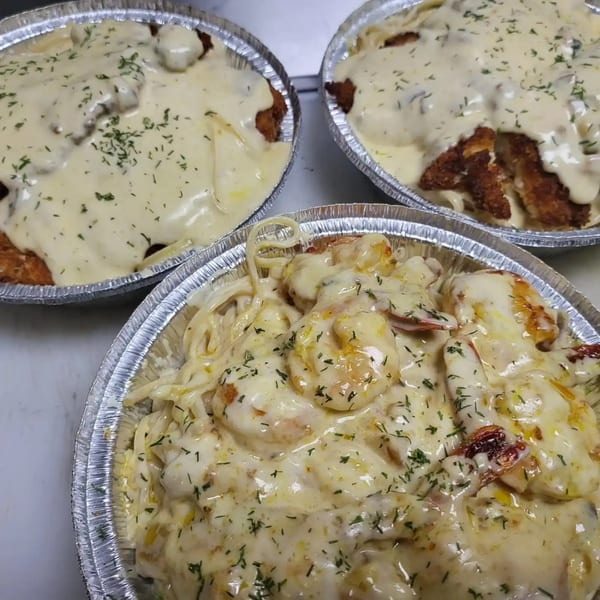 Three foil containers filled with creamy pasta dishes, two with chicken and one with shrimp.